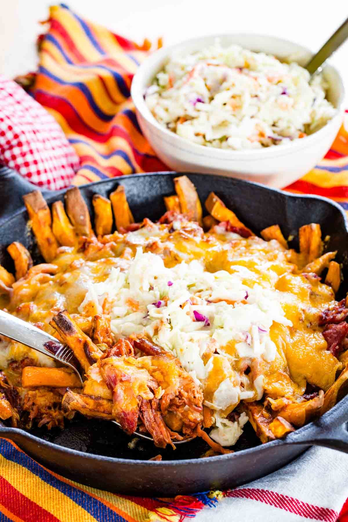 A serving spoon scooping up some BBQ pulled pork fries from a cast iron pan.