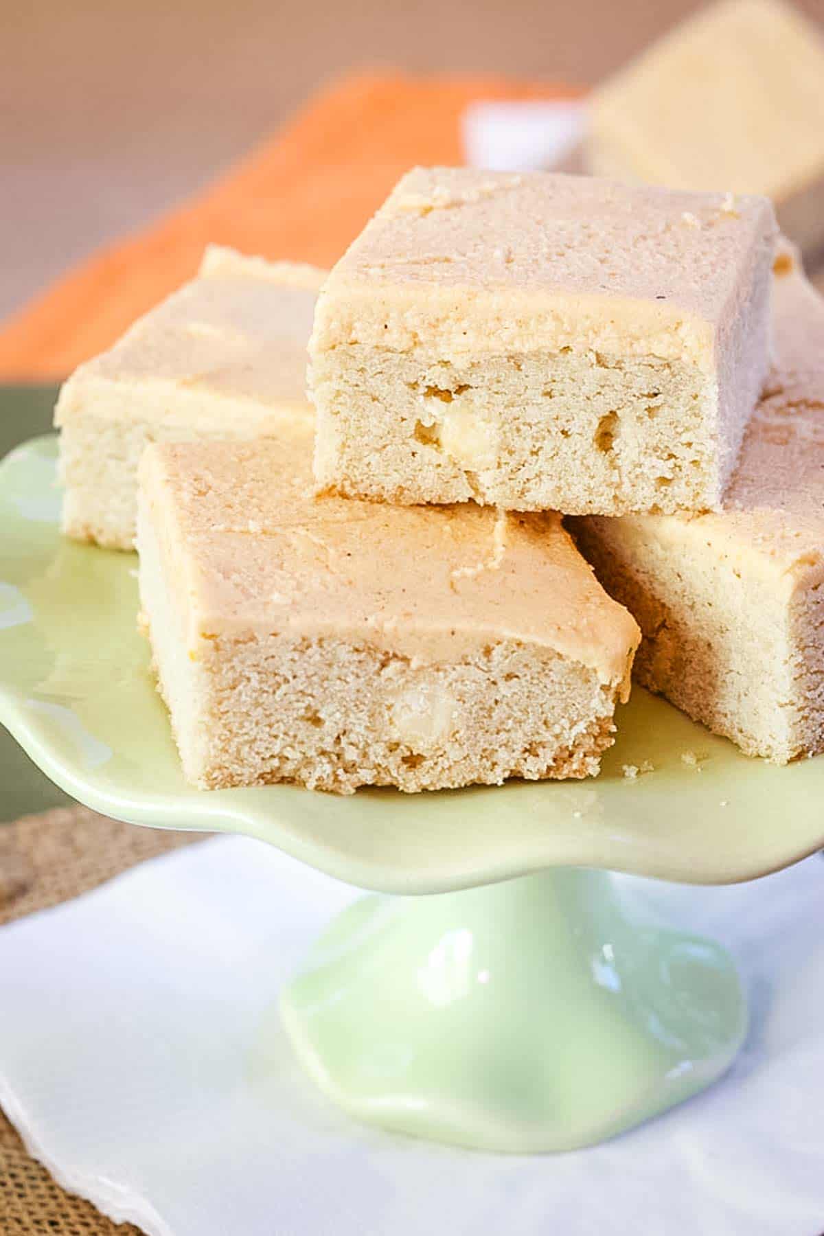 Pumpkin spice frosted cookie bars stacked on a green cake stand.