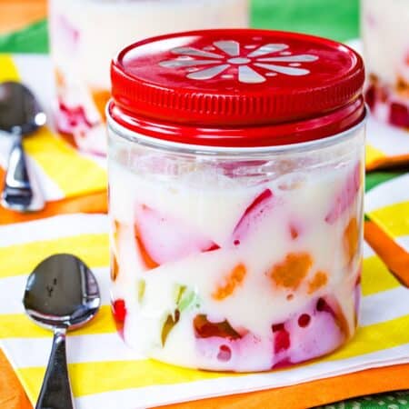 A rainbow jello parfait with colorful cubes and white gelatin in a jar with a red lid.