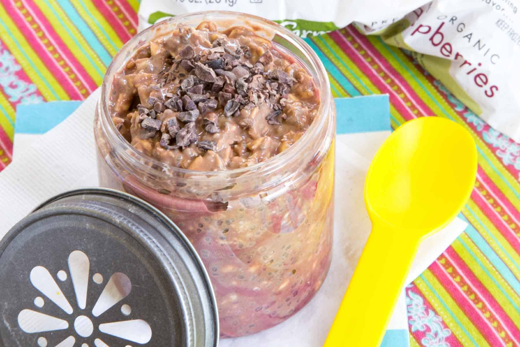 A jar of mocha overnight oats with cacao nibs on top and a metal lid leaning against it.
