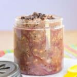 A small jar of chocolaty overnight oatmeal with the lid and a yellow spoon next to it with text overlay that says "Raspbery Mocha Overnight Oats".