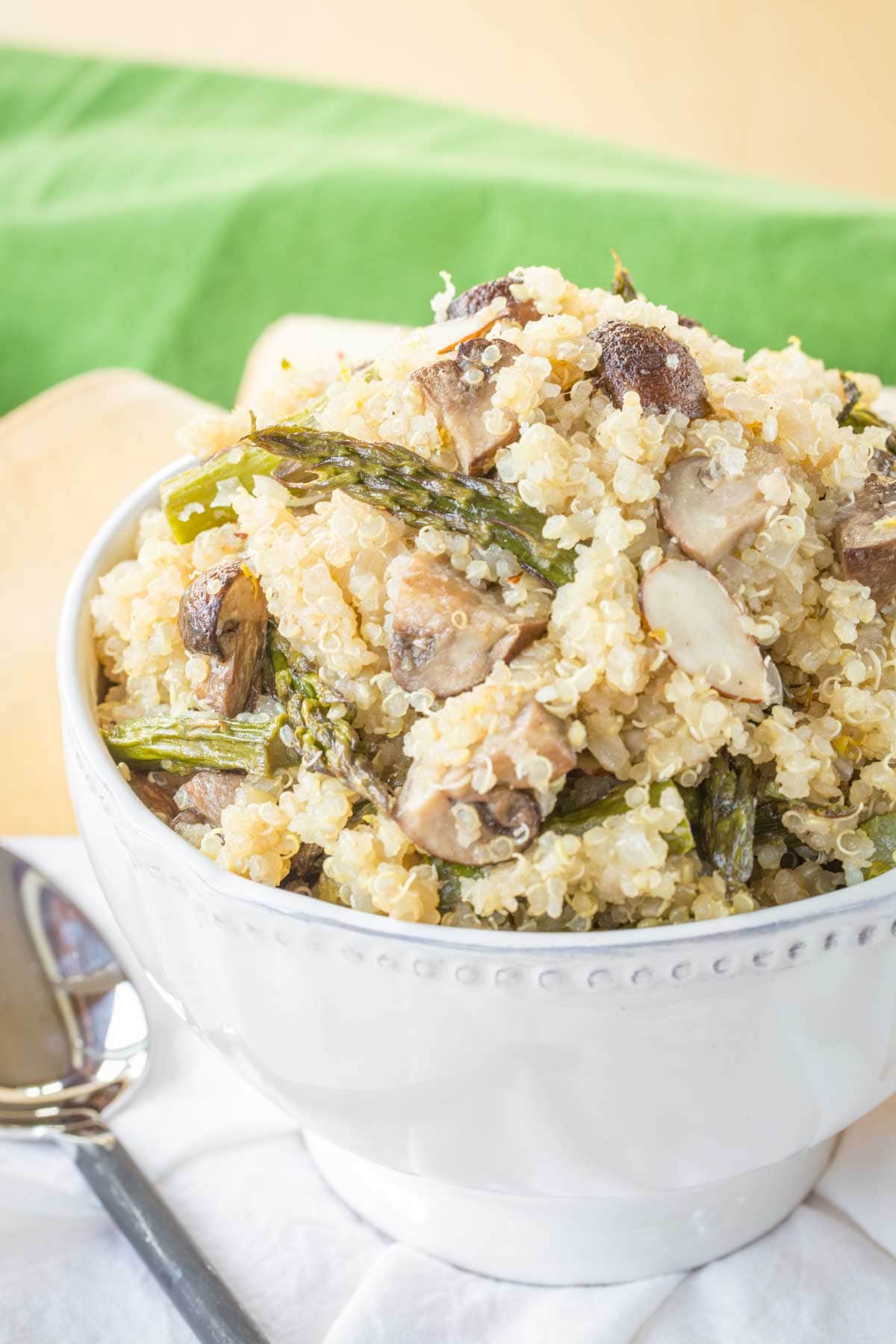 Quinoa Pilaf with roasted asparagus and mushrroms plus sliced almonds in a white serving bowl.