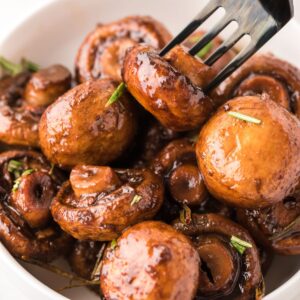 A fork poking into a bowl of balsamic roasted mushrooms.