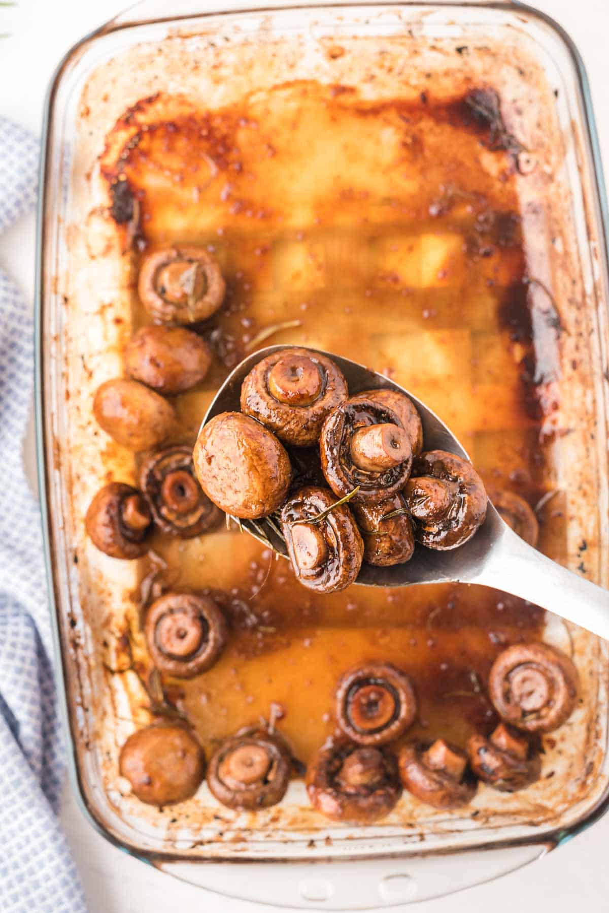 Serving spoon with roasted balsamic mushrooms from a baking dish.