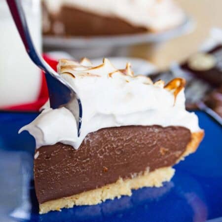 A fork digging into the corner of a slice of gluten-free s'mores pie on a blue plate.