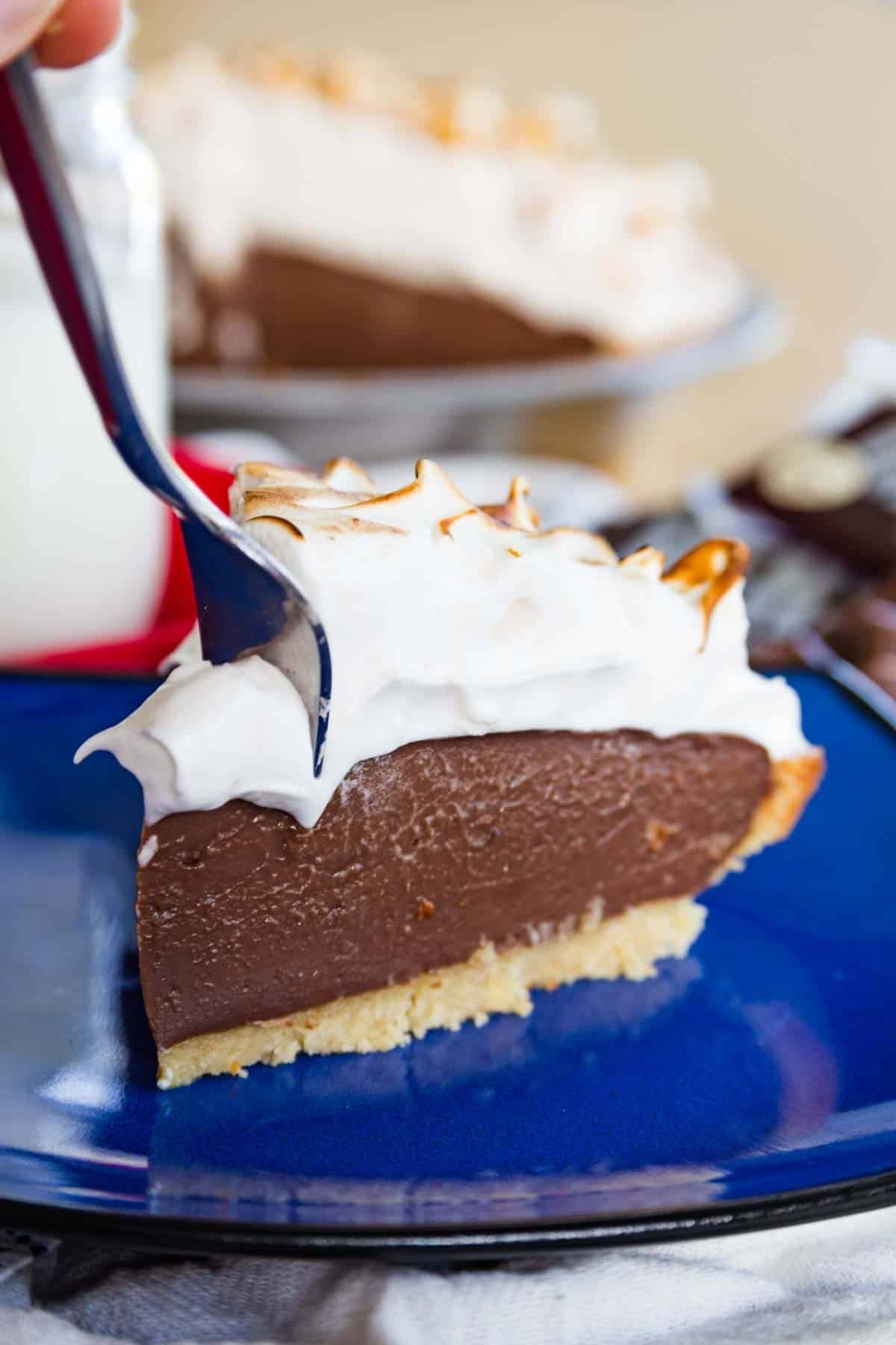 A fork digging into the corner of a slice of gluten-free s'mores pudding pie on a blue plate.