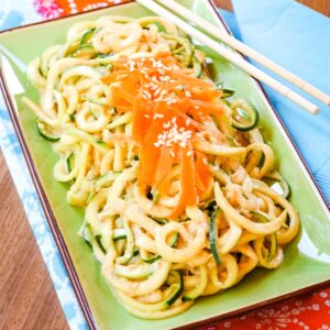 Cold Sesame Zoodles salad on a green plate with chopsticks on the corner on top of a brightly colored cloth napkin.