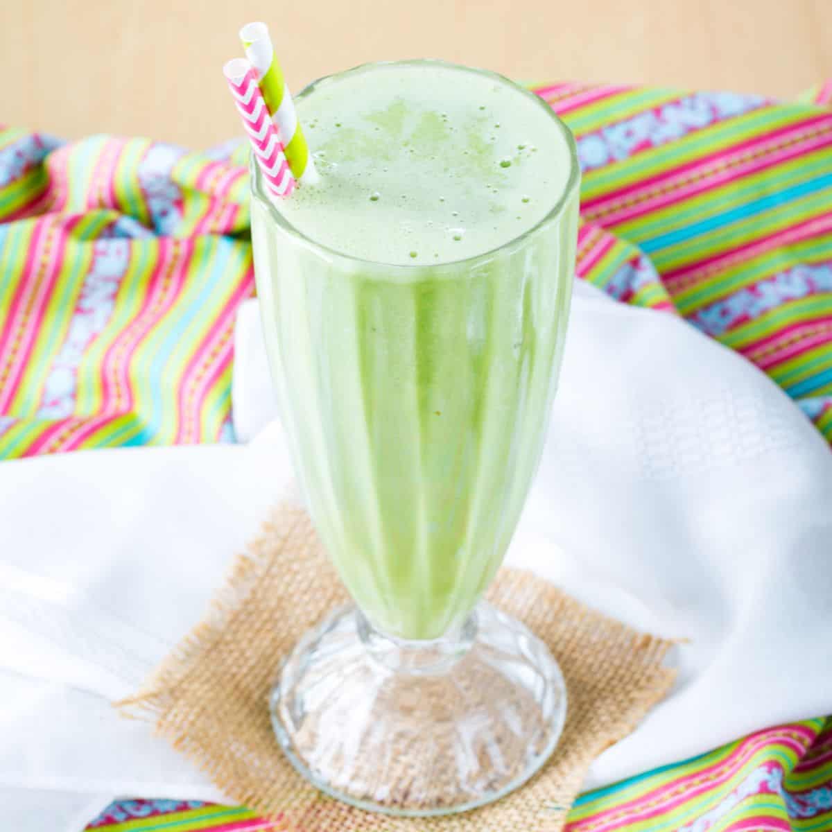 A green mint smoothie in a milkshake glass with two paper straws.