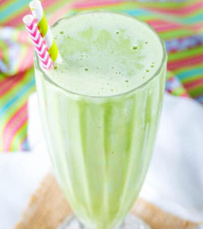 A green mint smoothie in a milkshake glass with two striped straws.