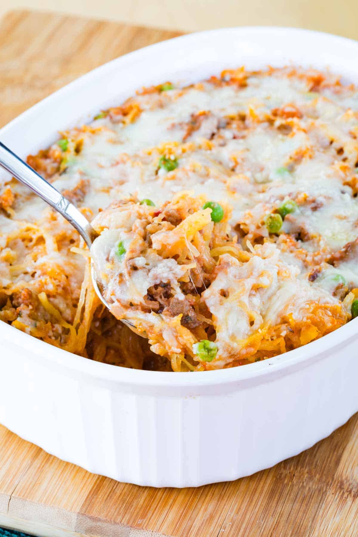 A spoon scooping up a serving of spaghetti squash casserole from a white baking dish.