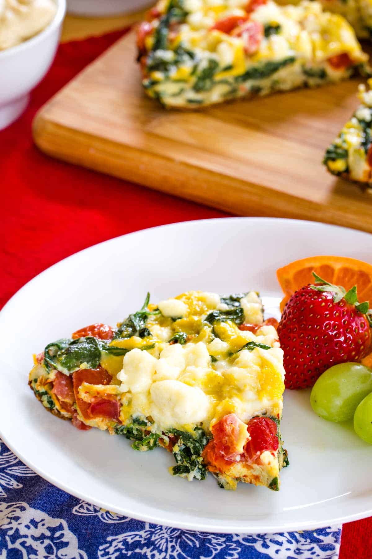 A slice of Spinach and Feta Frittata served on a white plate with fruit