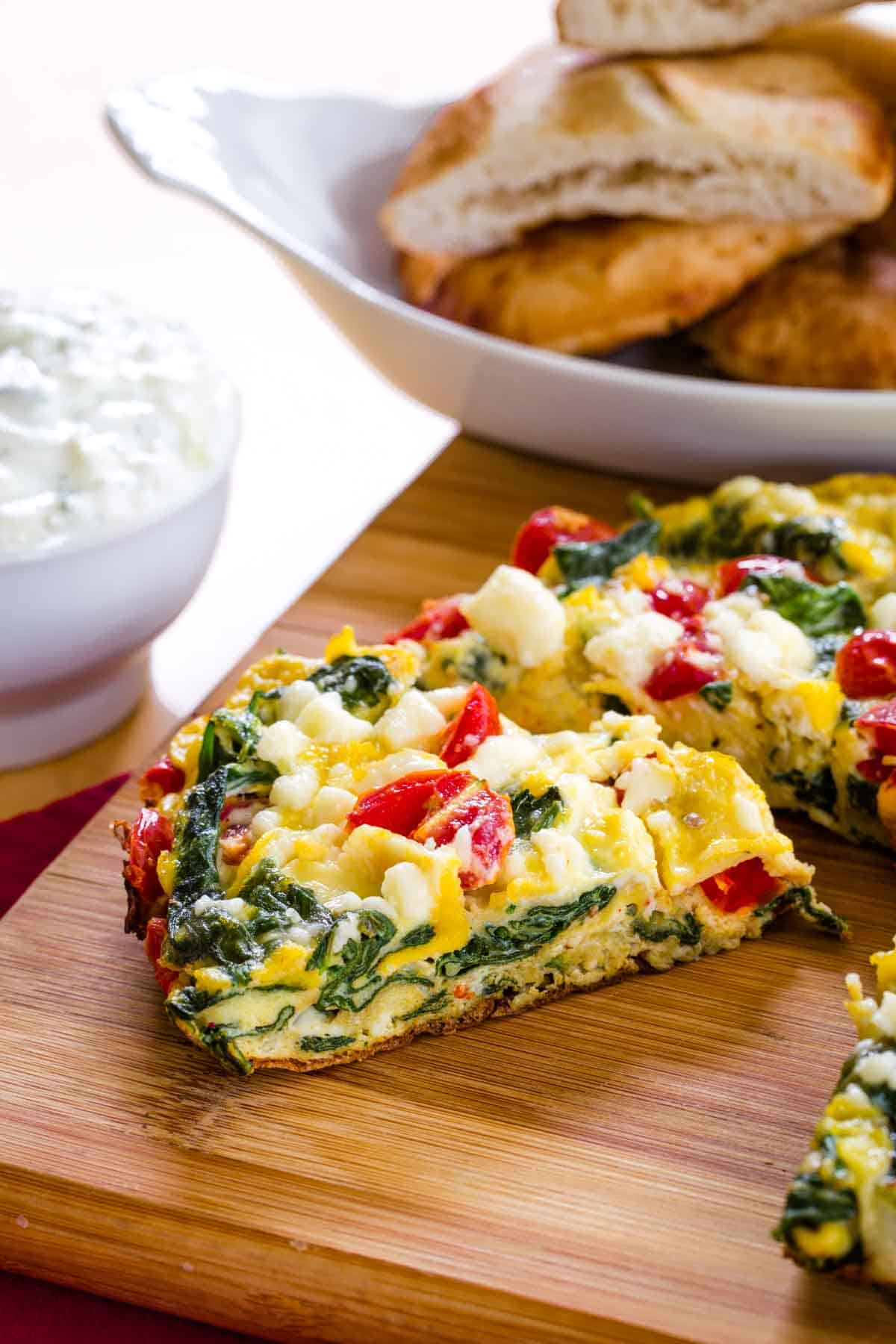 Tomato Feta Spinach Frittata being cut into pieces on a cutting board