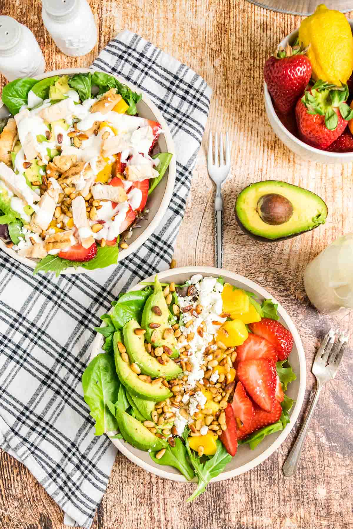 An overhead of two bowls of strawberry mango salad, one with chicken added.
