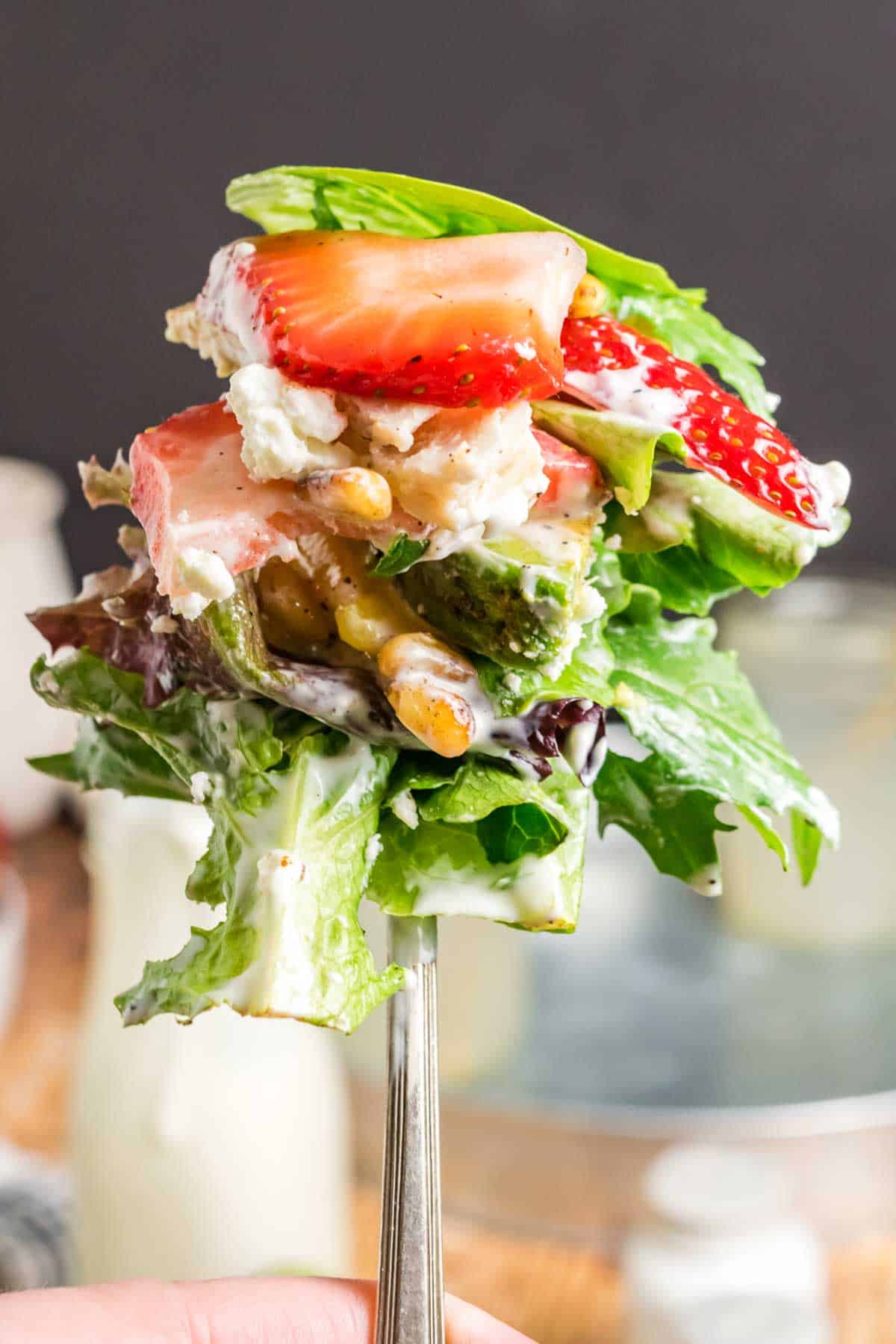 Fork holding a bite of the final tossed salad with strawberry slices.