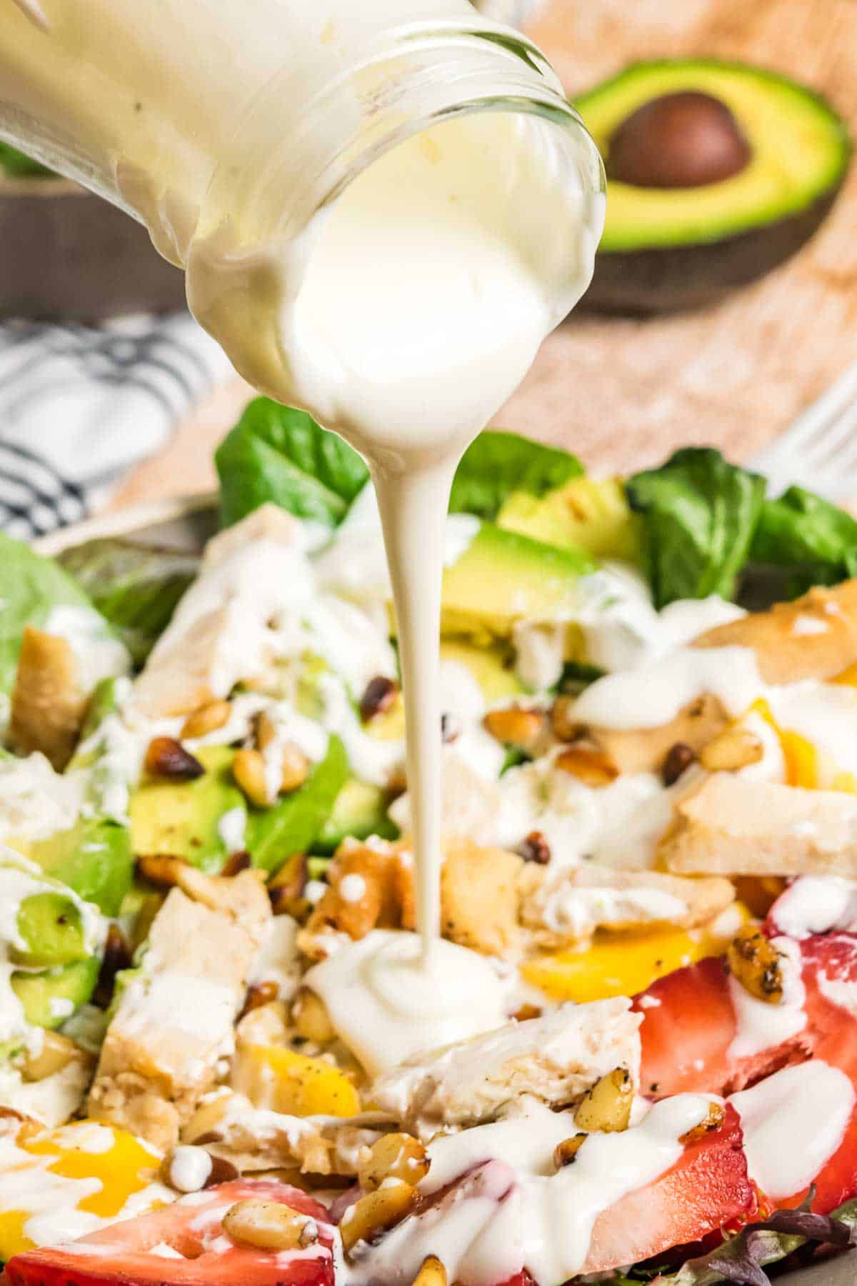 Pouring creamy salad dressing over the fruit and mixed greens salad.