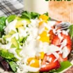 A bowl of salad with fruit, mixed greens, and creamy dressing with text overlay that says "Strawberry Mango Salad".