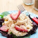 A plate of strawberry quinoa chicken salad on top of lettuce on a blue plate with a pink-handled fork.