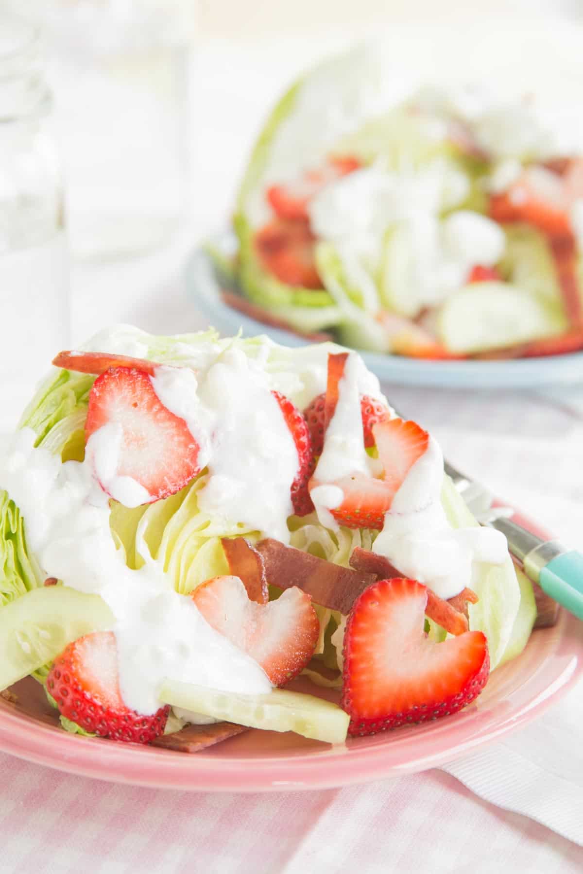 A strawberry wedge salad on a pink plate with another one blurred in the background.