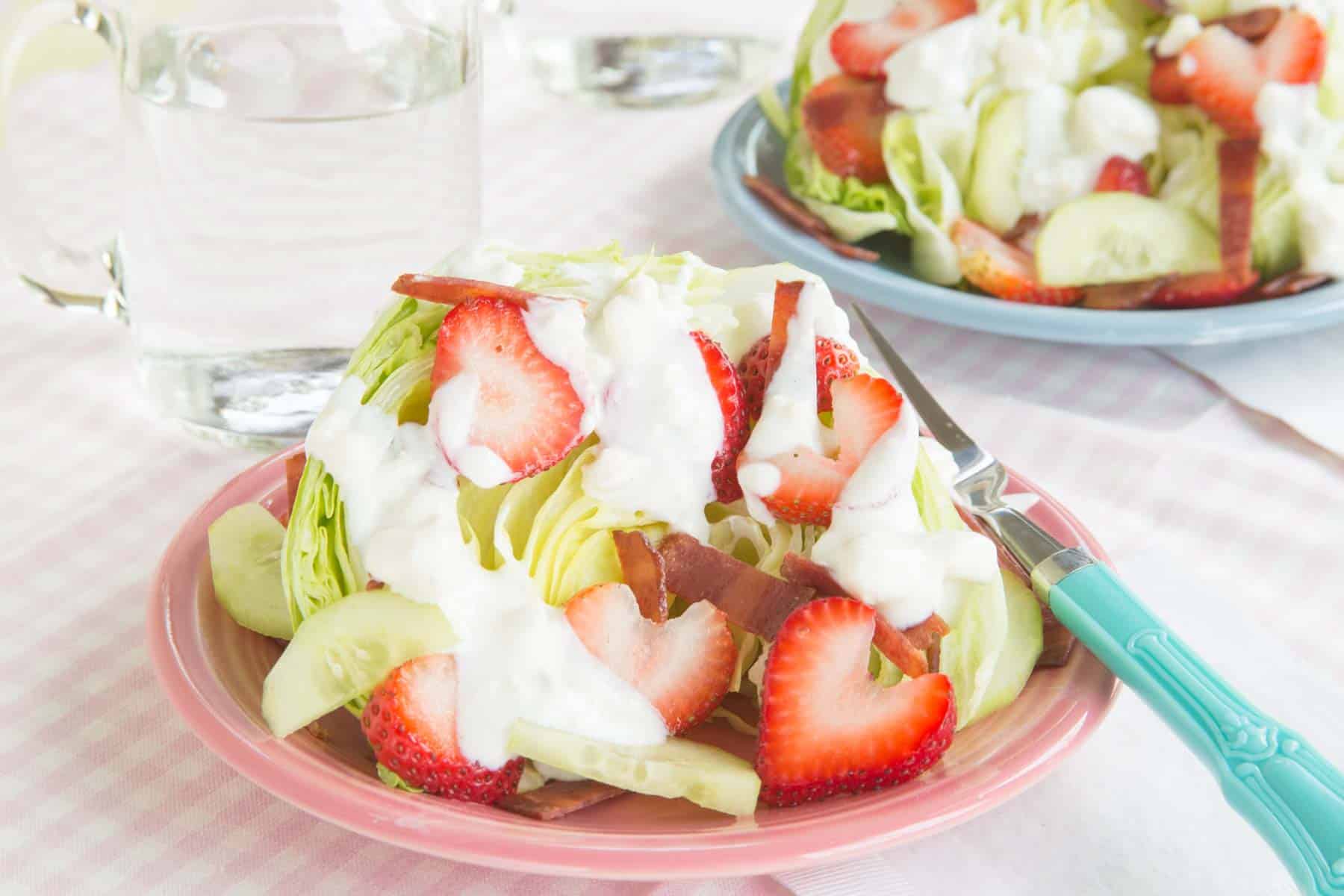 A wedge salad with strawberries on a pink plate with another on a blue plate in the background.