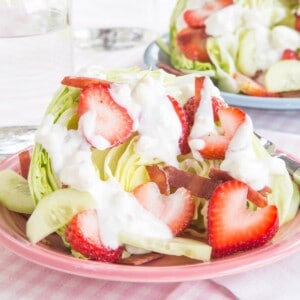 A wedge salad with strawberries on a pink plate.