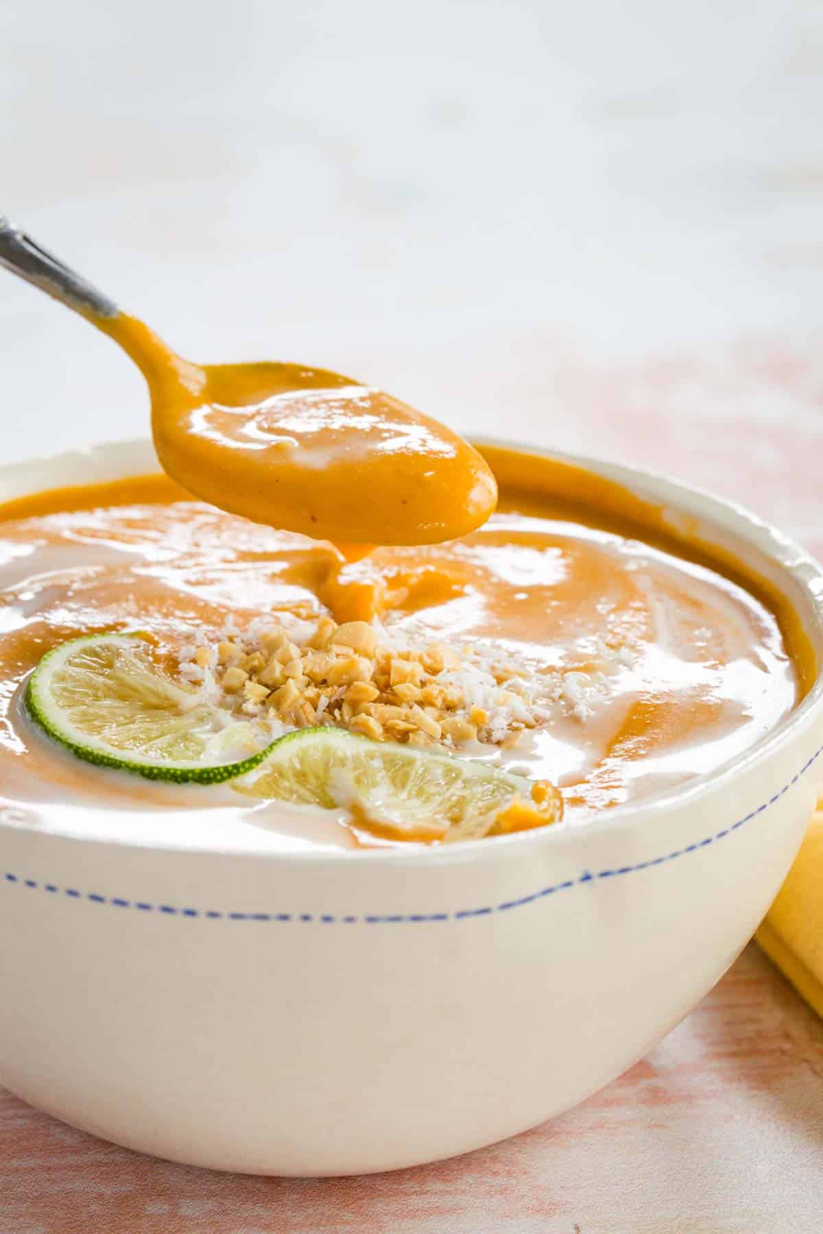 A spoon lifting some butternut squash soup out of a white bowl.