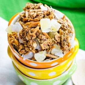 Looking down at tropical granola in an orange bowl stacked with yellow and green bowls.