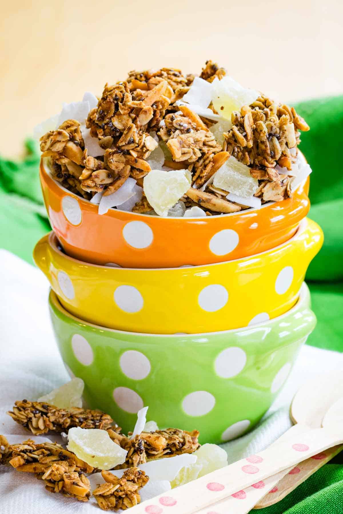 Three stacked bowls with tropical granola in the top one and a little spilled beside the bowls.