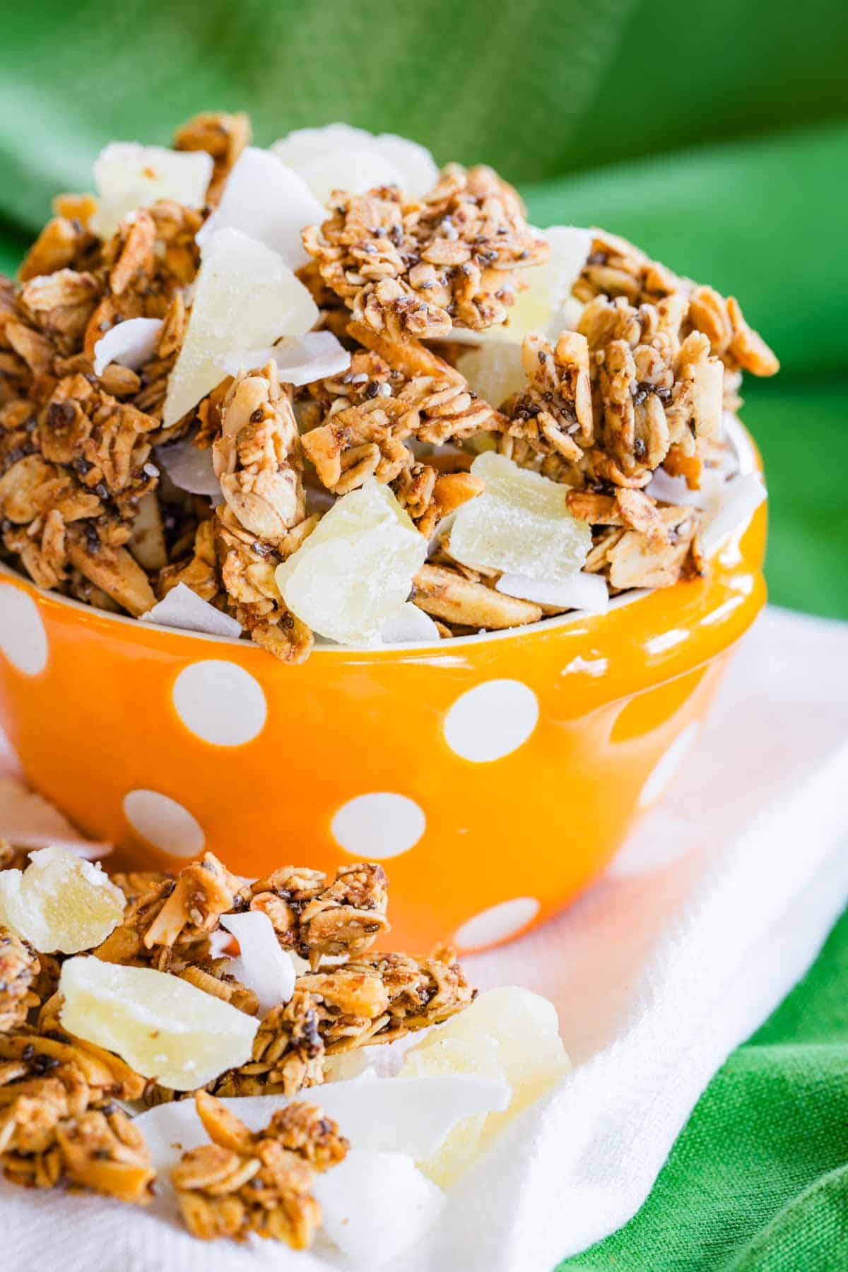 Granola with pieces of dried pineapple and coconut in an orange bowl with white polka dots.