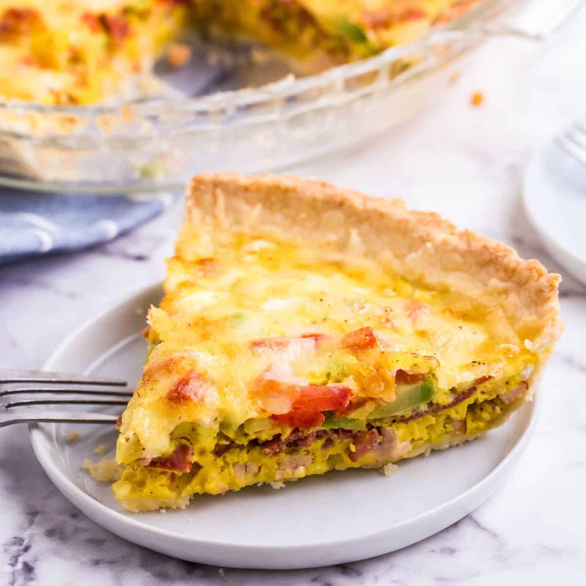 A slice of turkey quiche with bacon, tomato, and avocado on a plate.
