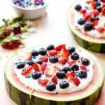 A round of watermelon topped with whipped cream, berries, and sprinkles and sliced like a pizza.