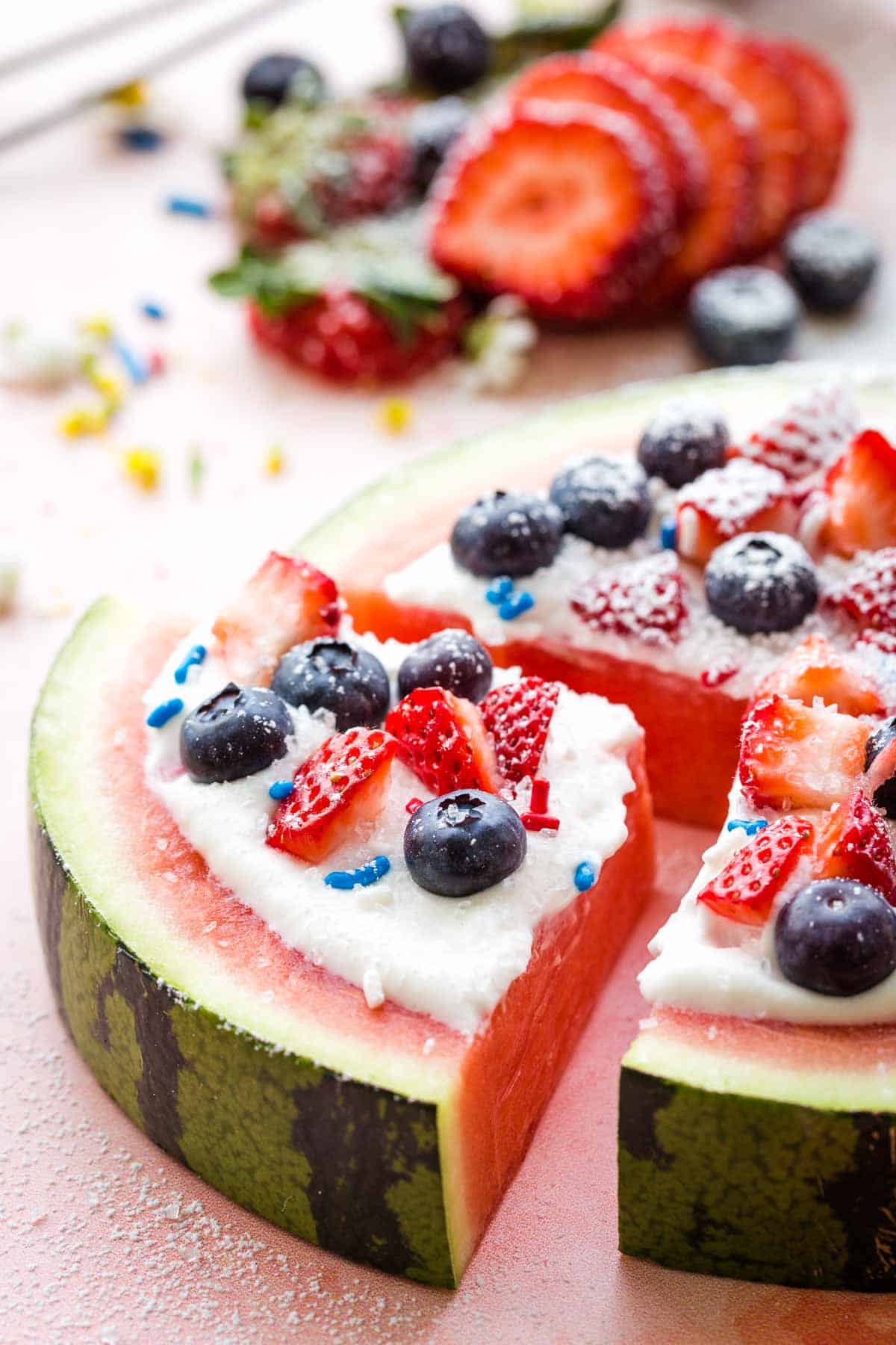 A slice of watermelon pizza with strawberries and blueberries and red, white, and blue sprinkles.