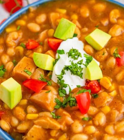 A closeup of a bowl of white turkey chili topped with avocado, sour cream, tomatoes, and cilantro.