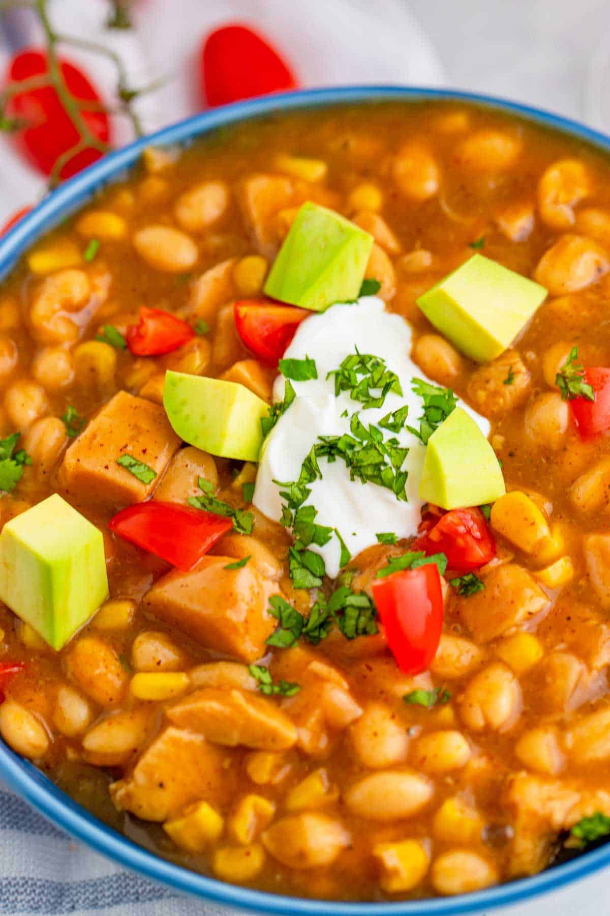 A closeup of a bowl of white turkey chili topped with avocado, sour cream, tomatoes, and cilantro.