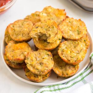 Zucchini tots piled on a white plate with a bite out of the top one.
