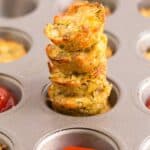 A stack of zucchini tots in one hole of a muffin pan and ketchup in the hole in front of them.