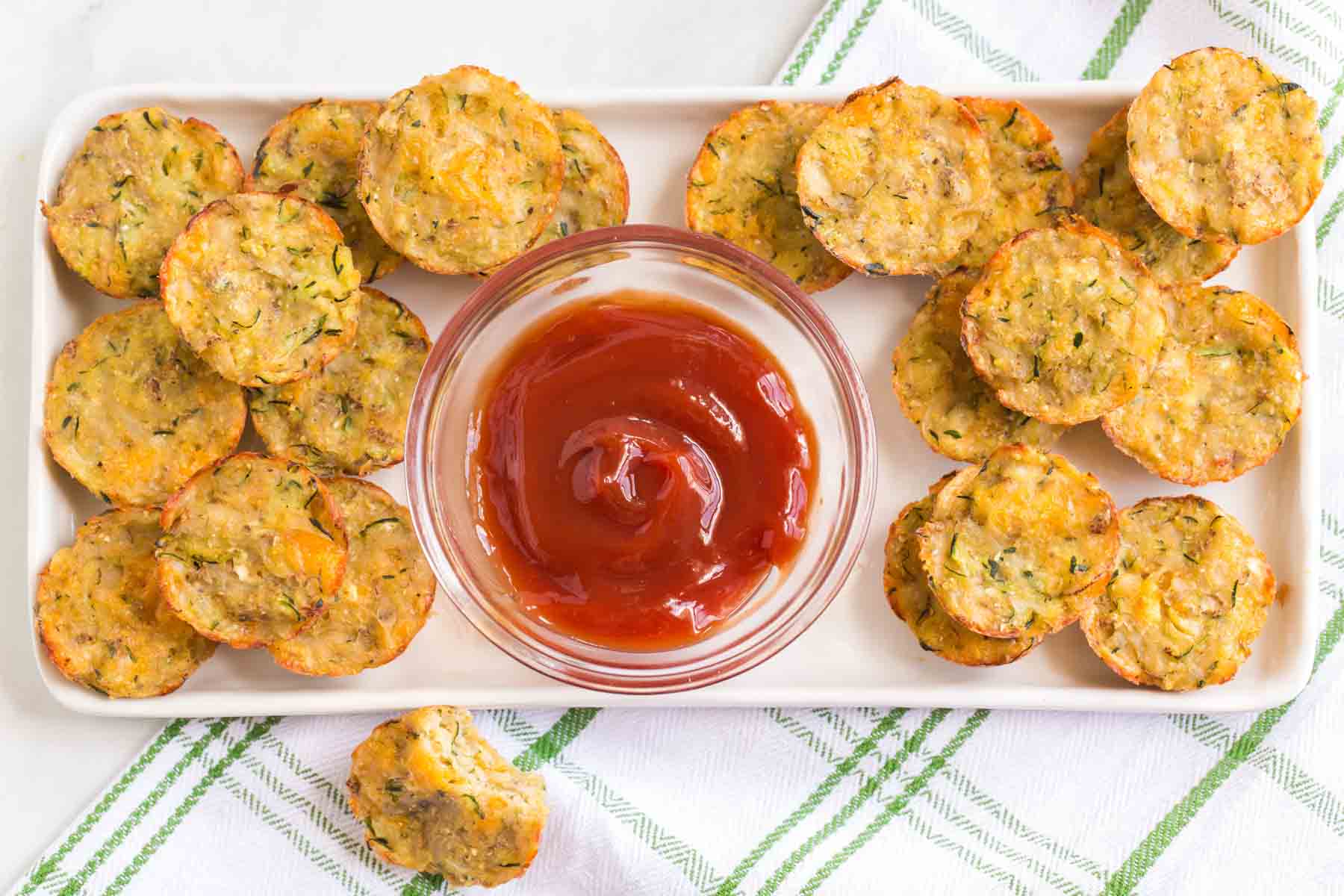 Zucchini Potato Tots on a rectangular platter with a bowl of ketchup.