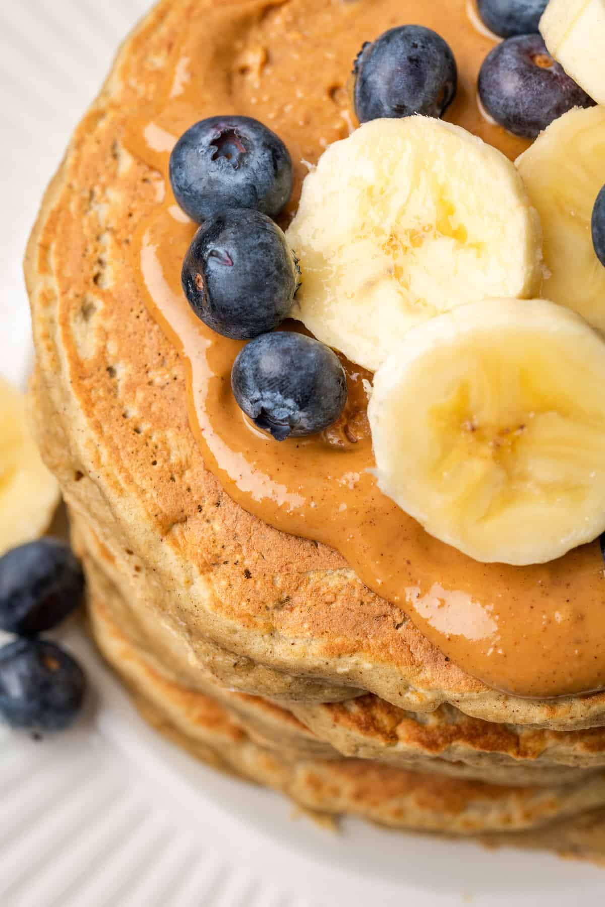 A close up photo of gluten-free protein pancakes topped with blueberries, sliced bananas, and peanut butter.