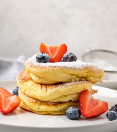 A stack of gluten-free souffle pancakes on a plate with fruit.