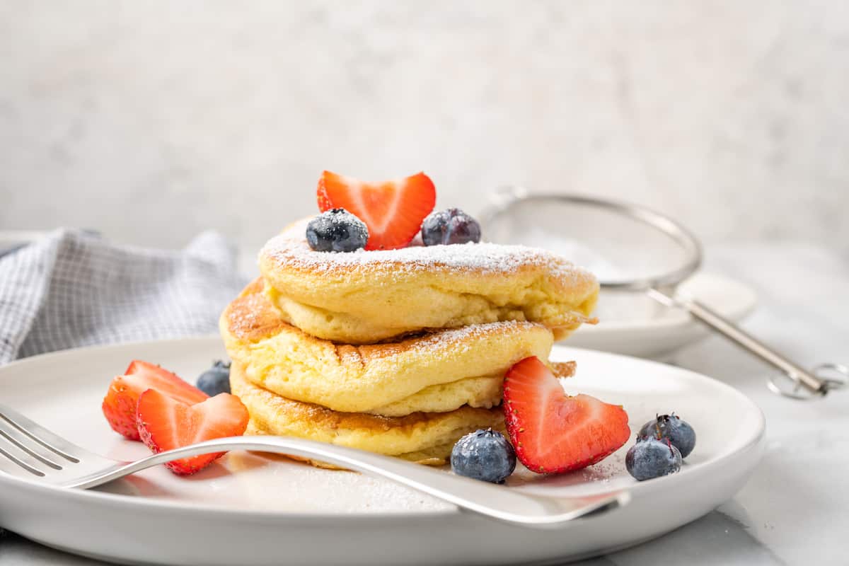 A stack of gluten-free souffle pancakes rests on a plate with fruit.