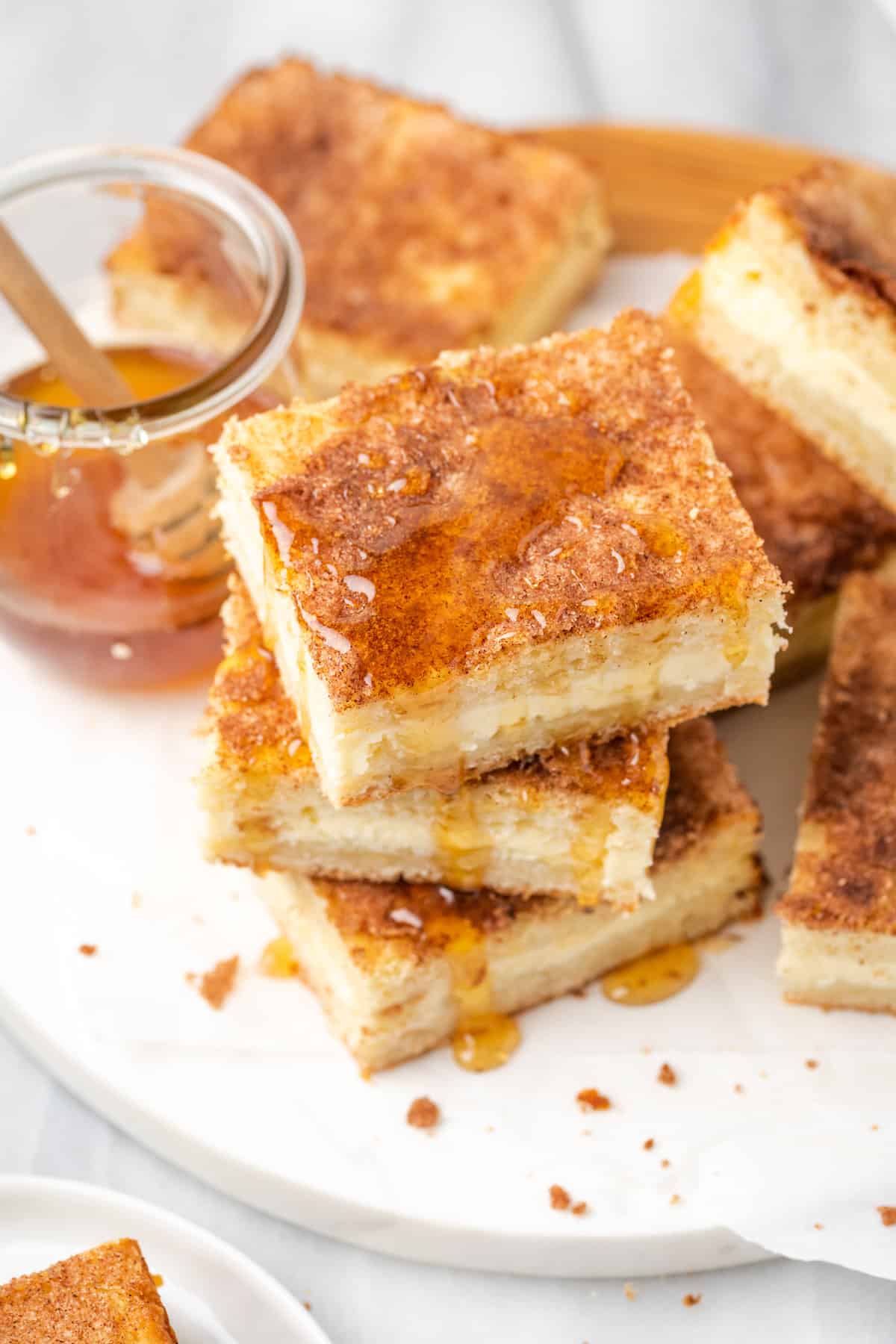 A stack of sopapilla cheesecake bars is shown on a plate drizzled with honey.
