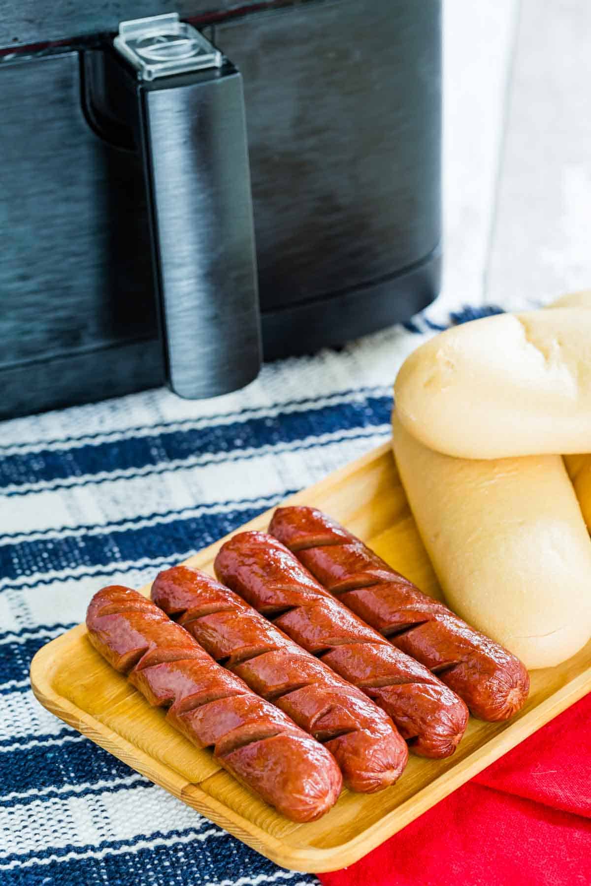 Cooked air fryer hot dogs are shown on a tray with buns on the side.