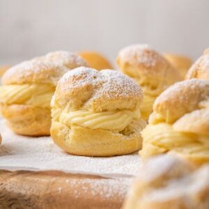 Gluten Free Cream Puffs dusted with powdered sugar on a wooden platter lined with parchment paper.