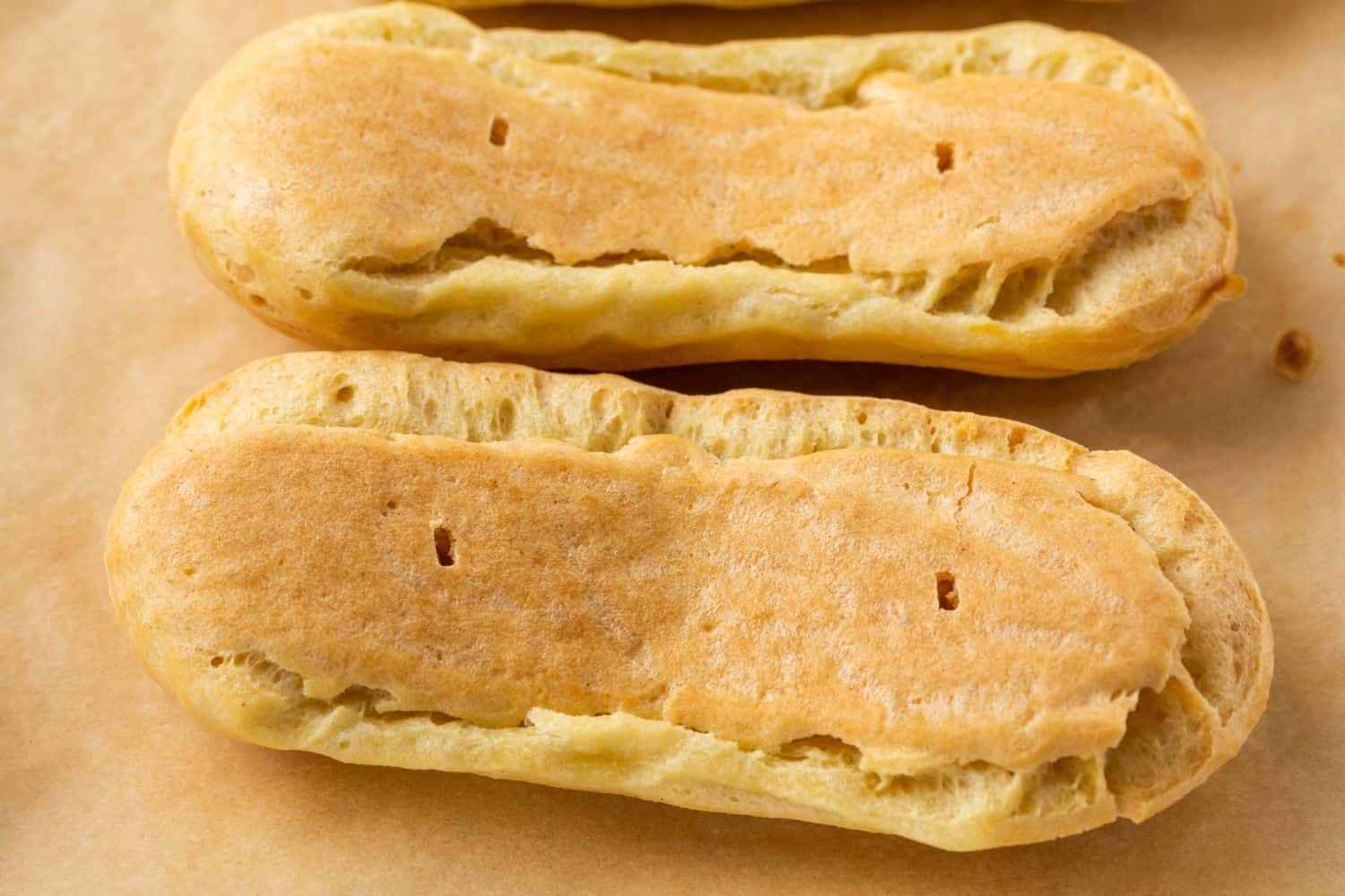 A couple of baked eclair pastries upside down on parchment paper.