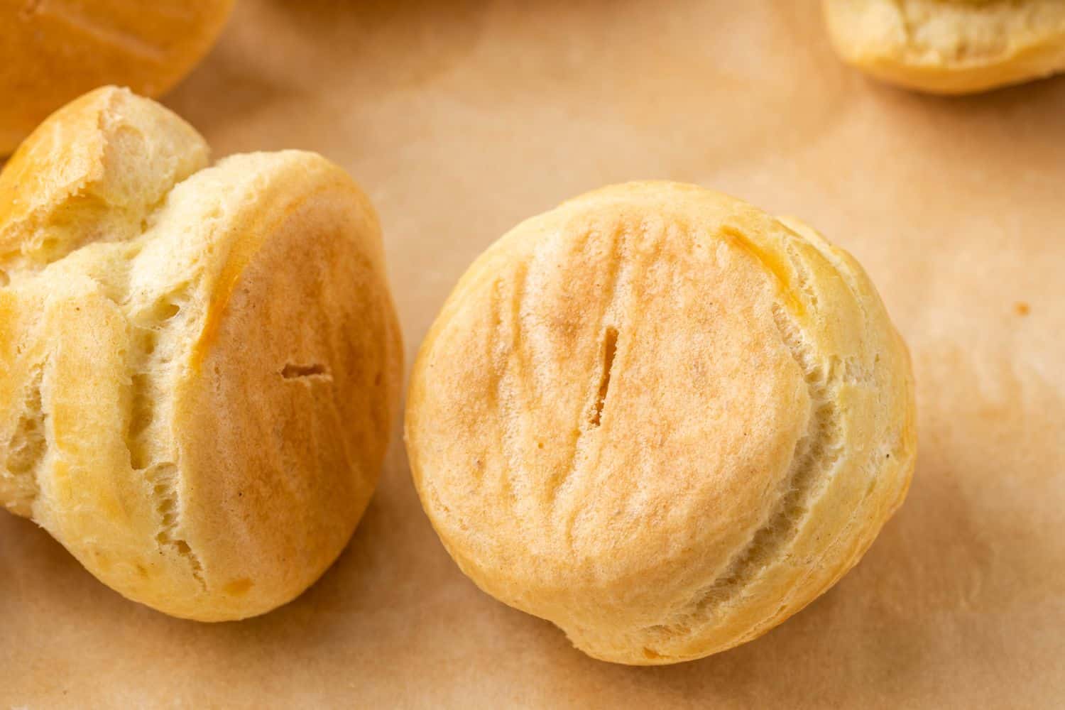 A couple of round baked choux pastries on parchment paper.