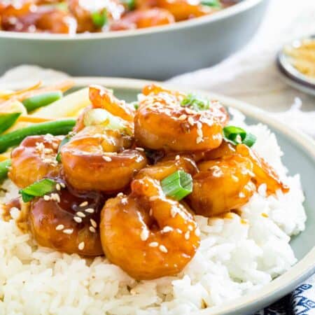 Teriyaki shrimp is shown on a bed of white rice on a plate.