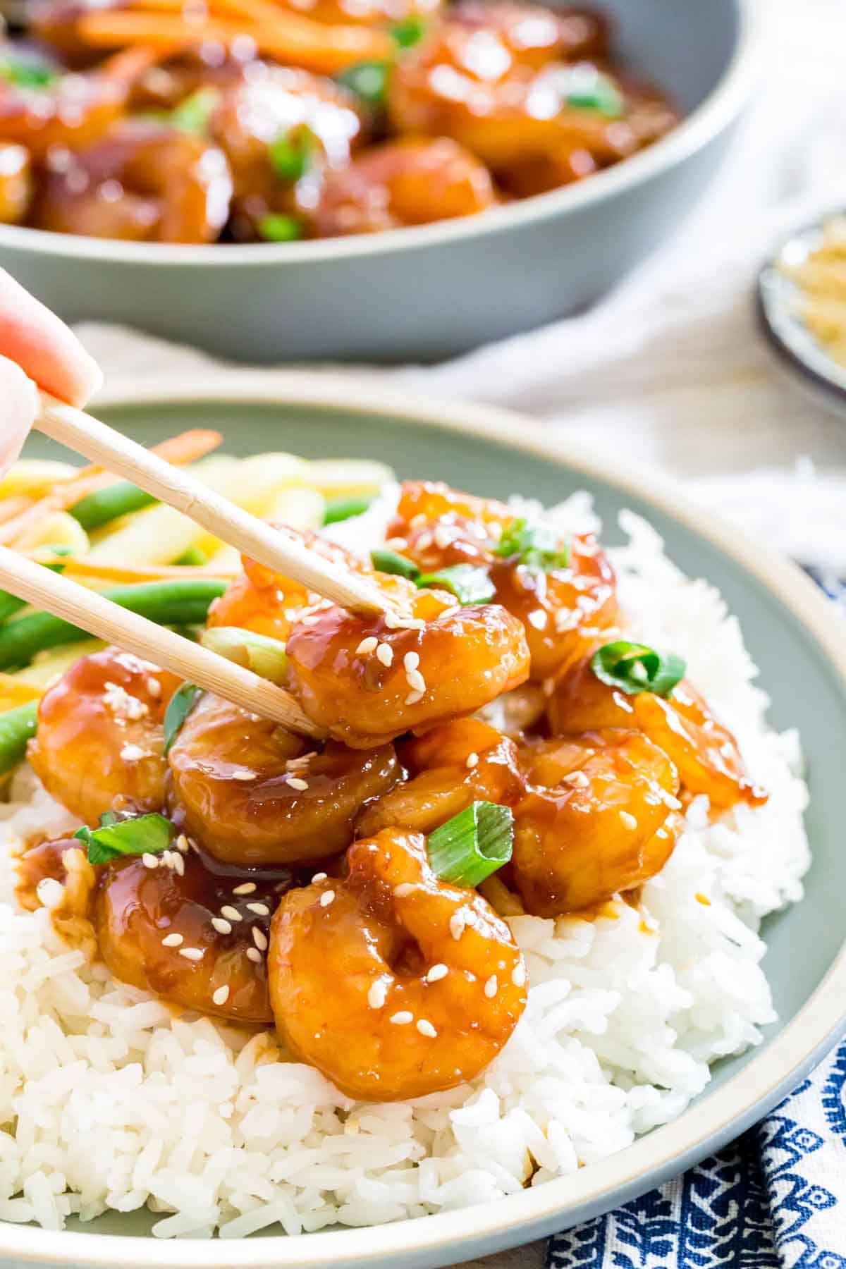 Chopsticks hold a piece of cooked teriyaki shrimp.