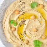 A bowl of hummus topped with olive oil and cilantro.