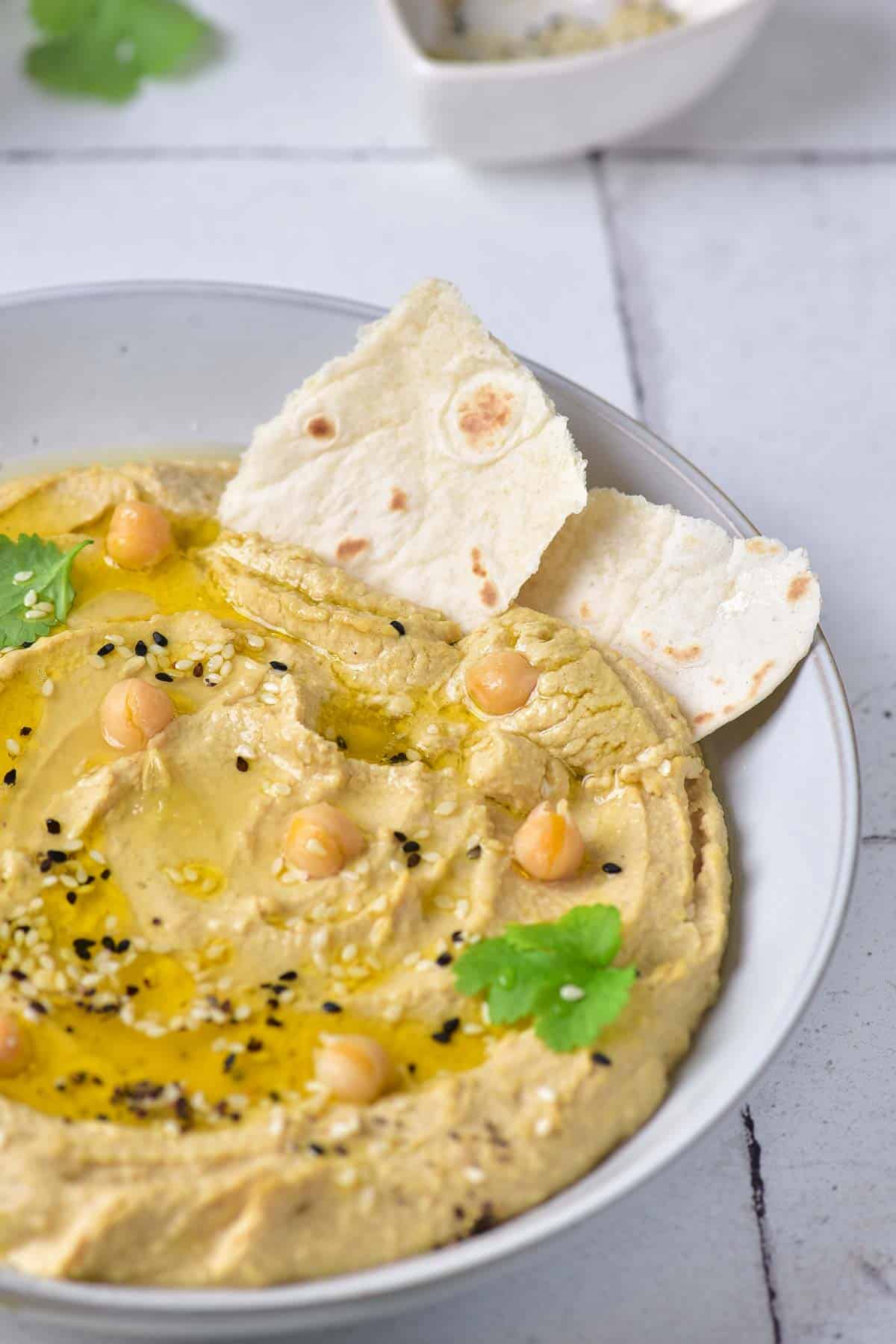 A bowl of hummus topped with olive oil and cilantro is served with pita bread.