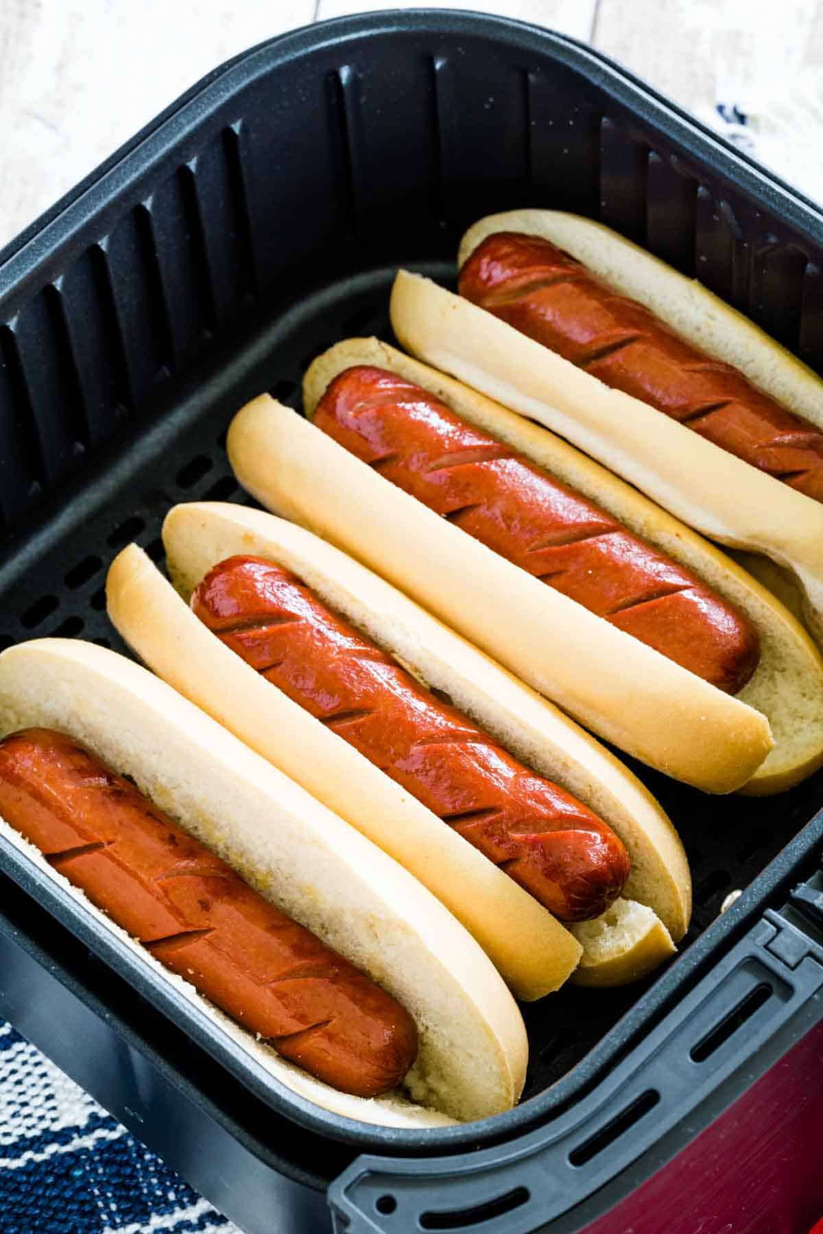 Hot dogs toast in buns in an air fryer.