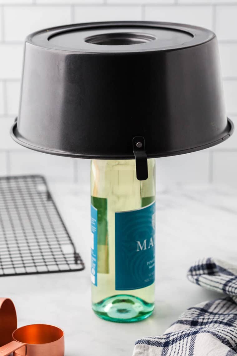 A tube pan with an angel food cake inside is inverted over a wine bottle.